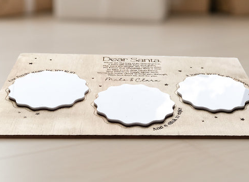 Close up of Flat-lay of engraved Santa treat board surrounded by cookies, milk, and holiday decorations for a Christmas Eve setup.