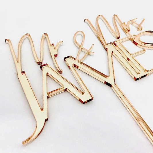 Elegant Gold Mr & Mrs personalised acrylic cake topper in modern calligraphy style, placed as a statement piece on a wedding cake. Customisable in colour options to match your theme, this topper is designed as a lightweight, durable keepsake. Perfect for weddings, engagements, or anniversaries, adding a romantic, stylish, and unforgettable finishing touch to the cake and overall event décor.