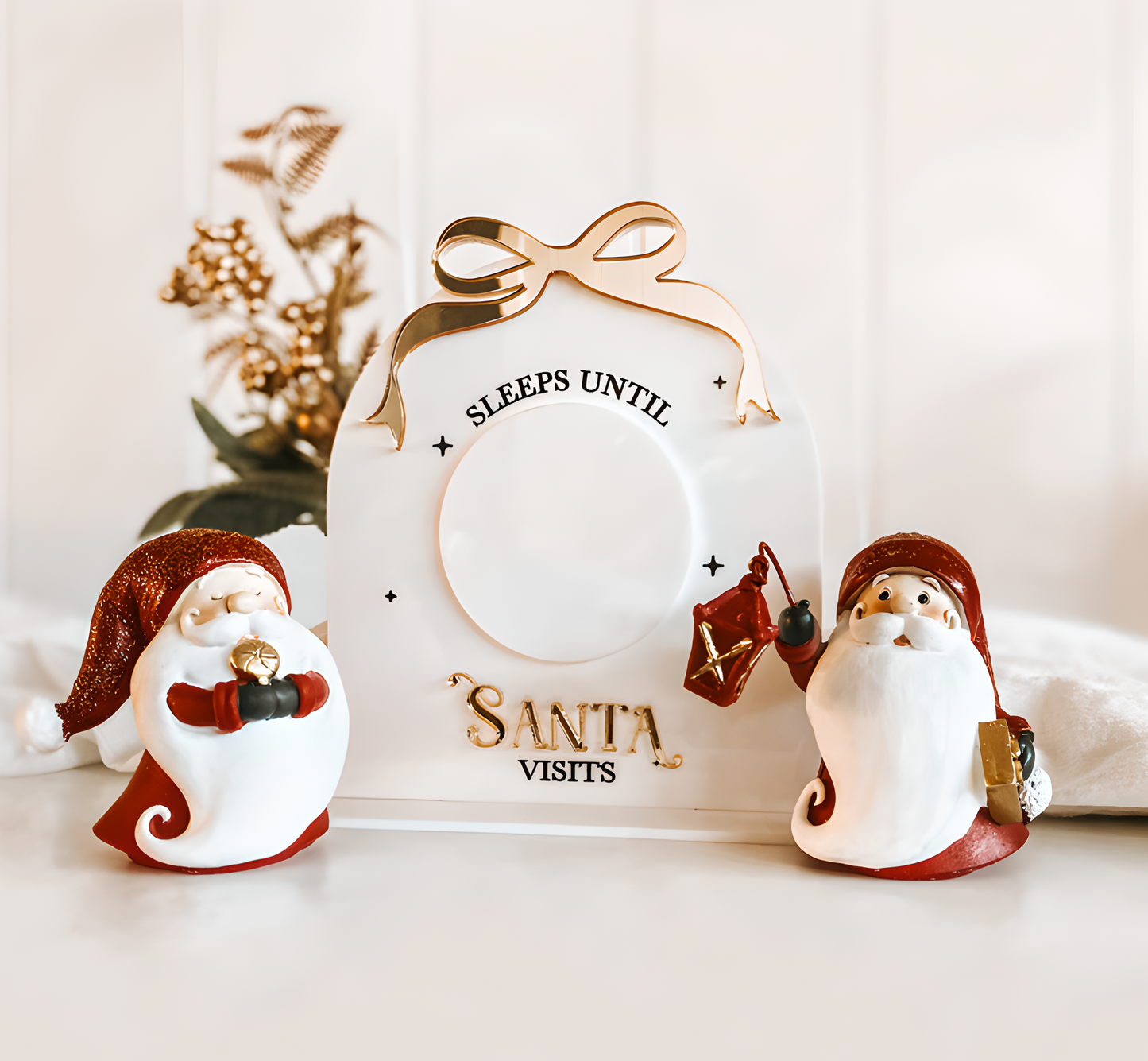 White acrylic Christmas countdown plaque with dry-erase circle and gold mirror bow accent, styled with white gifts and wreath.