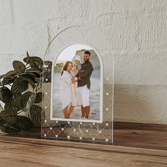 Decorative acrylic picture frame with a family photo on a wooden surface with a plant.
