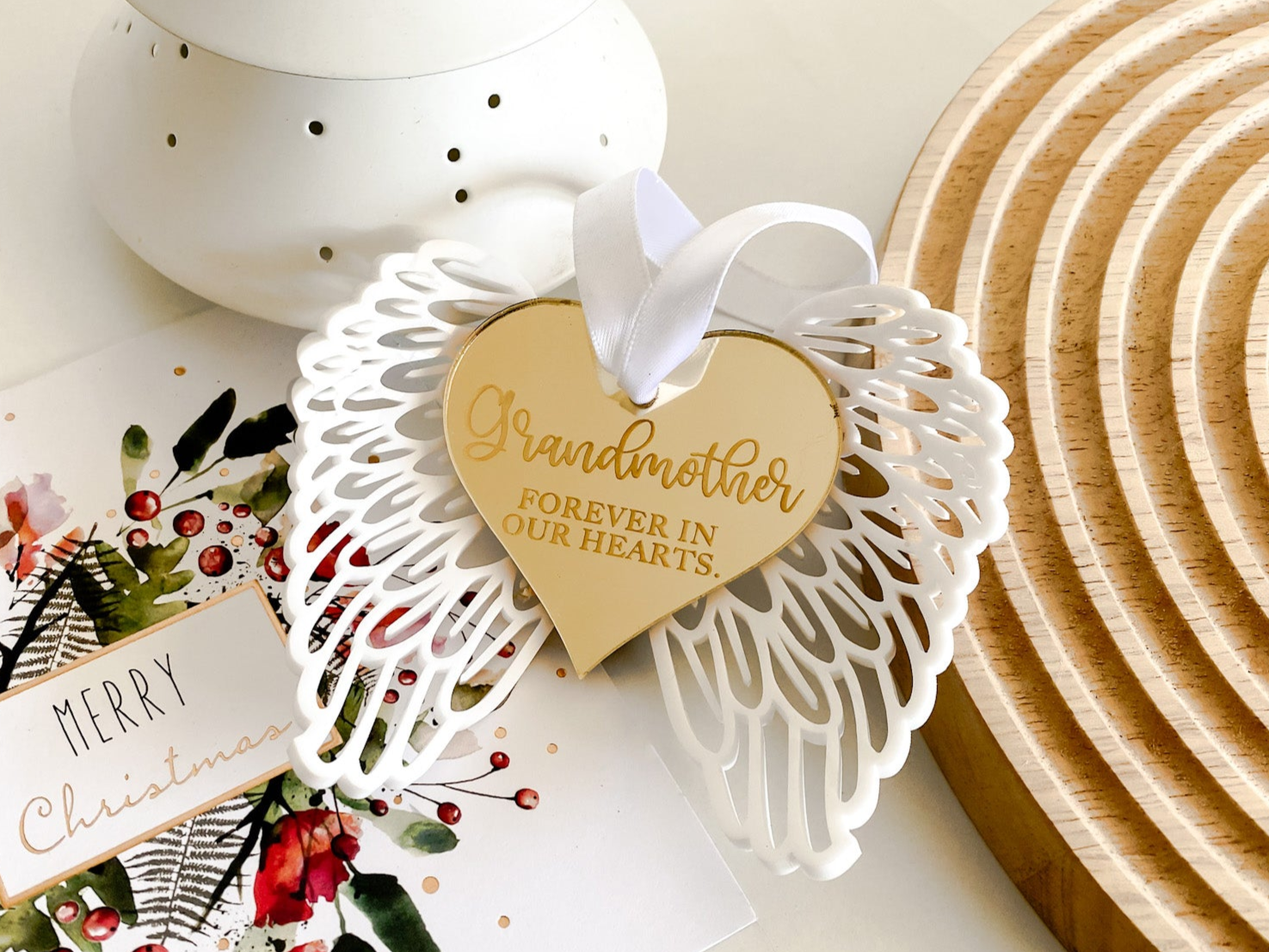 Custom remembrance angel wings Christmas decoration with engraved gold mirror heart, featuring the words “Grandmother – Forever in Our Hearts.” White acrylic wings with intricate cutout design, gold reflective heart centre, and white satin ribbon for hanging. A heartfelt sympathy gift, memorial keepsake, or tribute ornament to cherish loved ones during Christmas and holiday traditions.