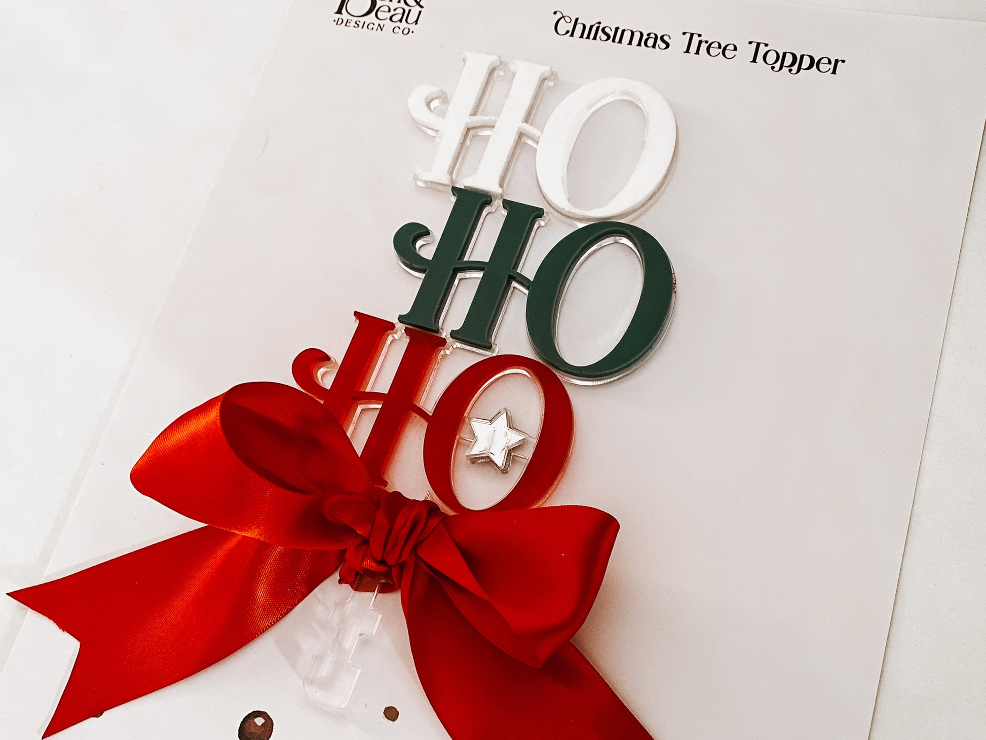 Handcrafted Acrylic Ho Ho Ho Tree Topper by Bell & Beau Design Co – a premium holiday decoration made from layered acrylic in Christmas colours, adorned with a luxurious red bow and silver star. Perfect for modern home Christmas décor or gift-giving.