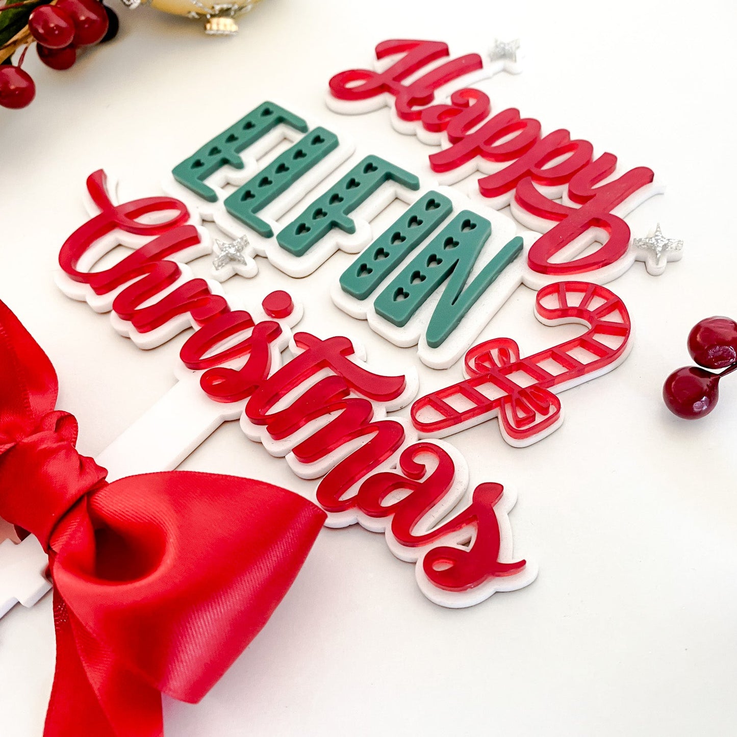 Handmade holiday tree topper by Bell & Beau Design Co. featuring laser-cut acrylic wording, luxurious red ribbon, and cheerful festive design.