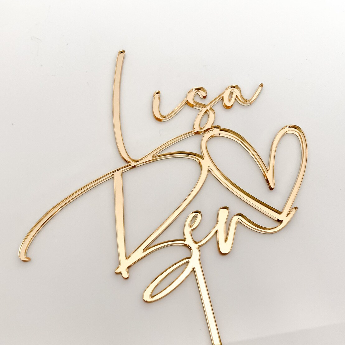 Romantic gold acrylic heart wedding cake topper, personalised to suit your wedding or engagement. Elegant and modern design adds charm and style to any cake, available in multiple colours for customisation. Durable yet lightweight acrylic ensures easy placement, making it perfect for weddings, anniversaries, or love-themed celebrations. Handmade in Australia, this topper is both décor and keepsake