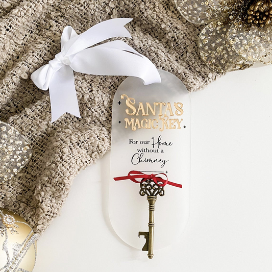 A beautifully styled Santa’s Magic Key acrylic sign in frosted white, featuring 3D layered gold lettering, black printed text, and a dainty red ribbon holding a vintage key. Finished with a white grosgrain bow for hanging — the perfect Christmas Eve tradition for homes without a chimney, handcrafted by Bell & Beau Design Co.