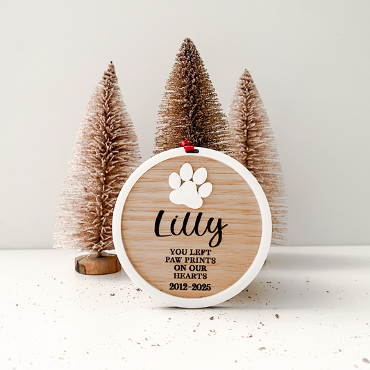 Decorative plaque with paw print design and text in front of small Christmas trees on a white background