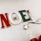 Modern acrylic Noel tree topper handcrafted by Bell & Beau Design Co, featuring layered red, white, and green acrylic letters with a bright red bow for easy tree attachment. A stylish holiday statement piece designed to complement both classic and contemporary Christmas themes.