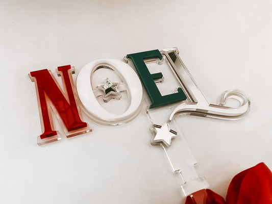 Modern acrylic Noel tree topper handcrafted by Bell & Beau Design Co, featuring layered red, white, and green acrylic letters with a bright red bow for easy tree attachment. A stylish holiday statement piece designed to complement both classic and contemporary Christmas themes.