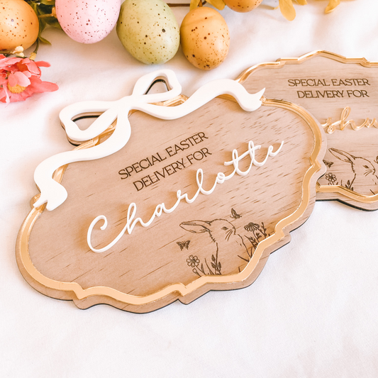 A top-down "flat lay" image of the Easter sign surrounded by soft ribbons, pastel eggs, and spring greenery. This image emphasizes the trending coquette design elements, showcasing the 3D white bow as the focal point of the personalized plaque.