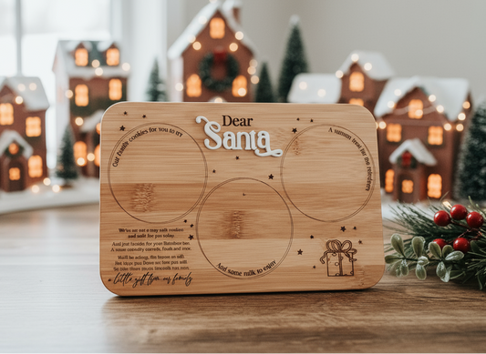 Wooden Santa treat tray engraved with “Dear Santa”, featuring designated circles for cookies, milk and reindeer treats. Handcrafted bamboo board on rustic wooden background with Christmas greenery — a sentimental Christmas Eve keepsake by Bell & Beau Design Co. Perfect for family traditions and festive photo styling.