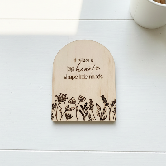 Flat-lay of engraved wooden arch magnet with floral border and heartfelt quote, perfect teacher appreciation piece.
