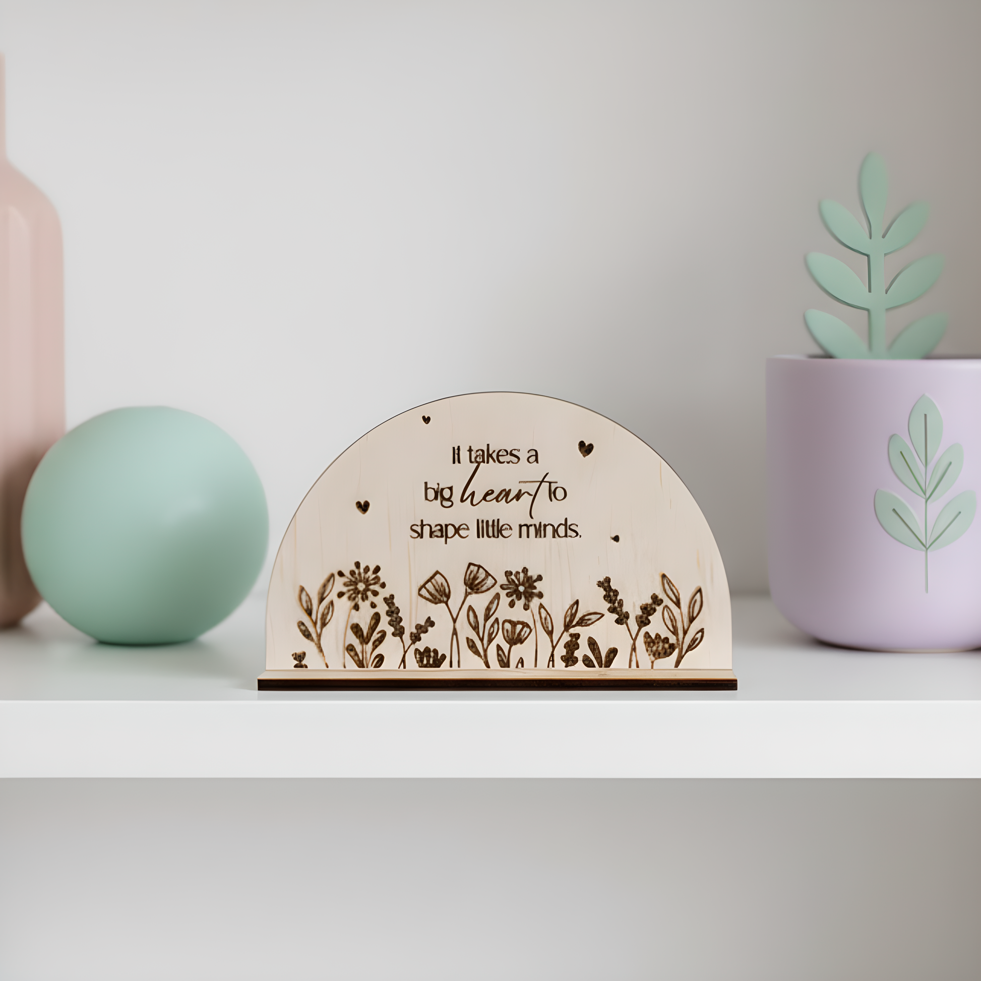 A wooden arch desk plaque with the quote "It takes a big heart to shape little minds" and space on the back for a custom message.