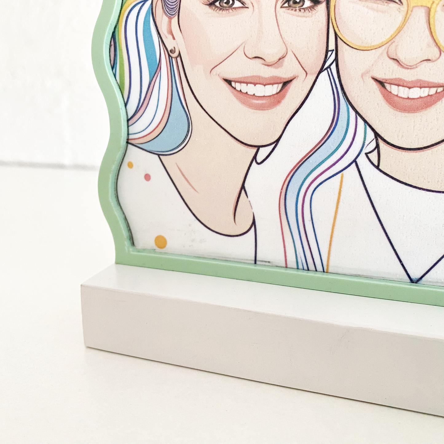 A bespoke custom portrait in a wavy light green frame, serving as unique desk decor on a white shelf.