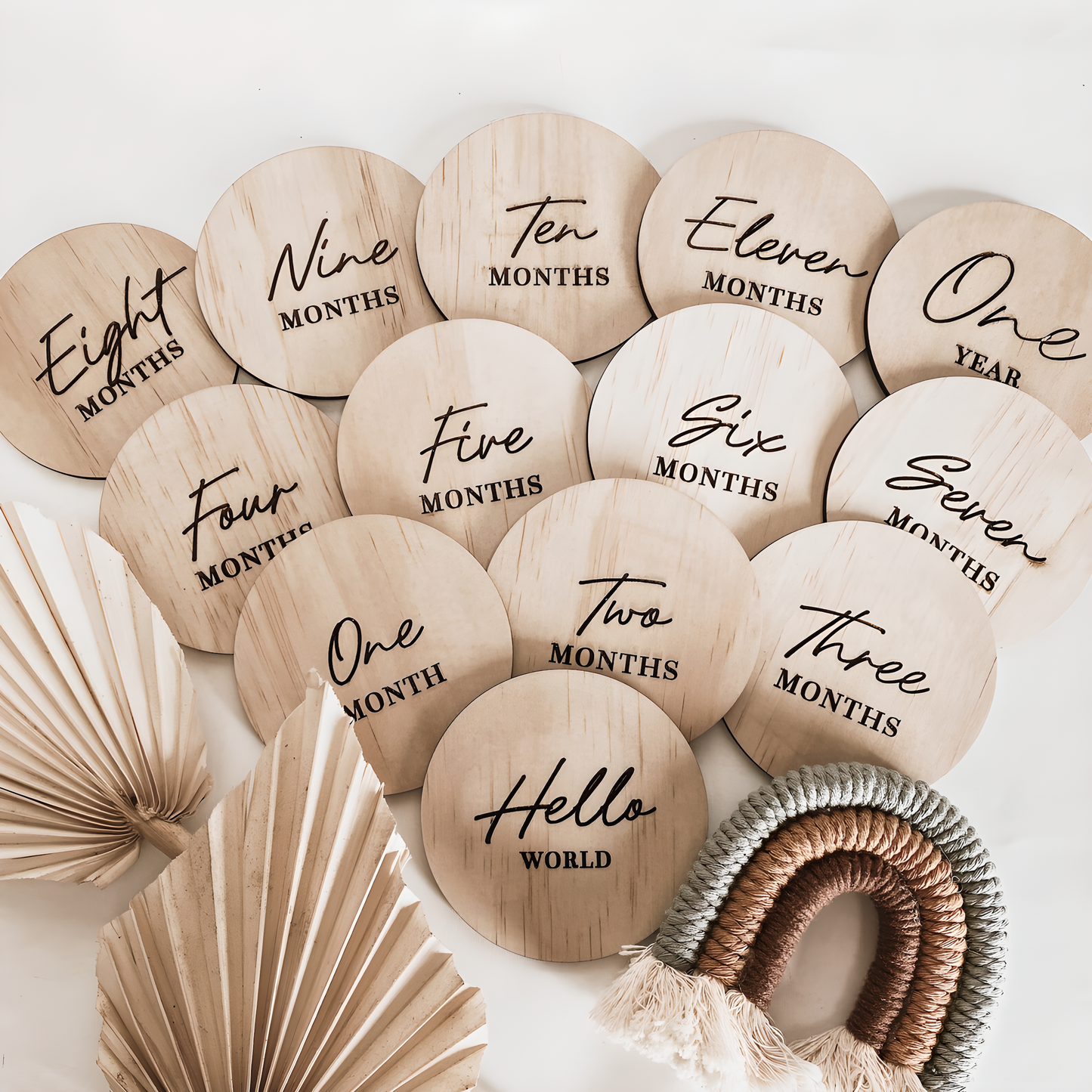 view of a full set of wooden baby milestone discs scattered on a white sheet with dried palm leaves.