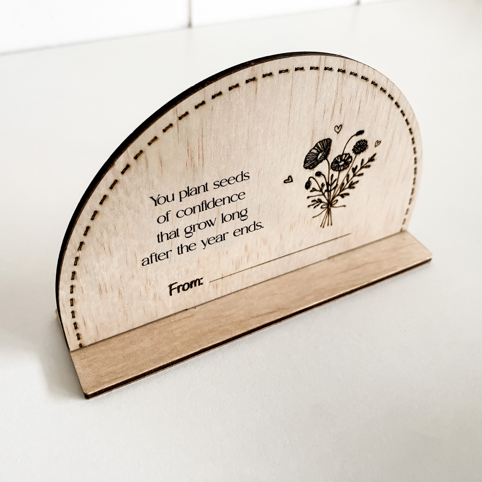 Detail of the precise laser engraving on a plywood teacher gift, including text and a bouquet illustration.