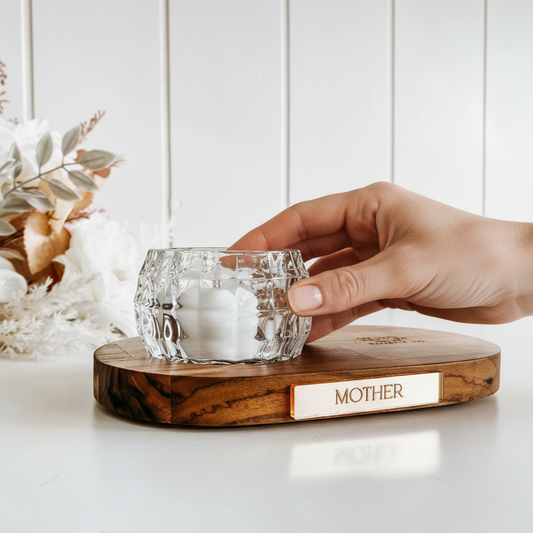 Hand holding a glass of ice on a wooden coaster with 'Mother' engraved, against a white background.