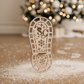 The wooden Santa's Boot Stencil standing upright on a timber floor, surrounded by white powder creating a trail of clear Santa footprints leading towards a blurred, beautifully decorated Christmas tree.