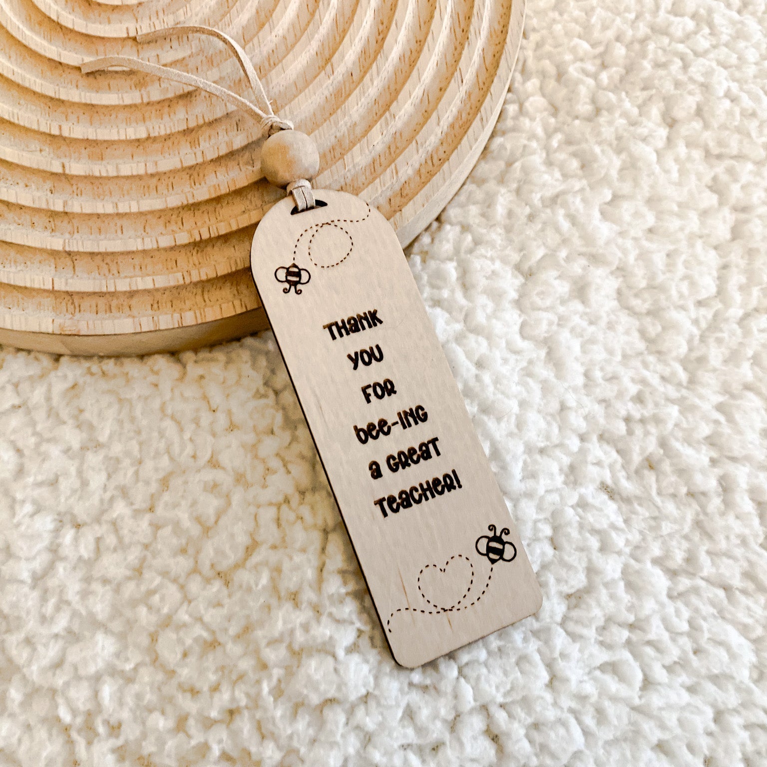 A wooden bookmark with a bee theme, "Thank you for bee-ing a great teacher!" engraved, on a textured background.