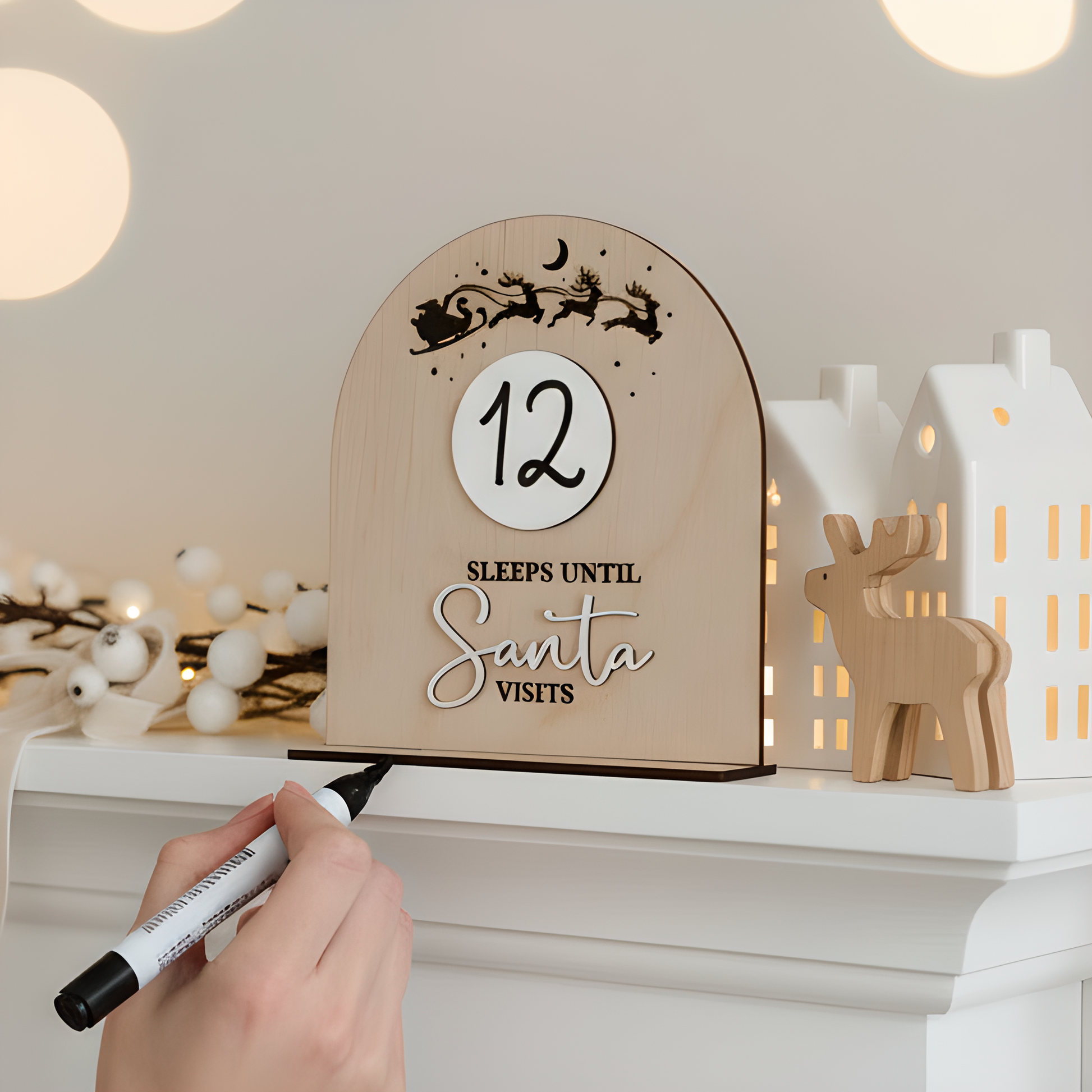 Wooden Christmas countdown sign with '12 sleeps until Santa visits' on a mantel with decorative lights and reindeer.